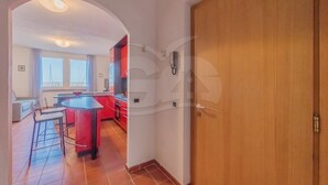 Una cocina amplia con armarios rojos, un comedor con mesa y sillas, y vistas de la ciudad a través de grandes ventanales.