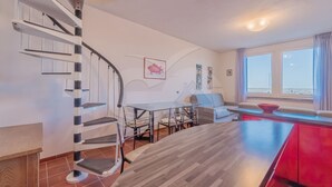 Un apartamento moderno con una escalera de caracol, comedor, cocina y sala de estar con vista al mar.