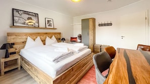 A bedroom with a wooden bed, a bedside table with a lamp, a chair, a small table, and a mirror. - Smart Resorts - Haus Topas - Ferienwohnung 302 mit 1 Schlafzimmer, Max. 4 Personen - Smart Resorts (Winterberg)