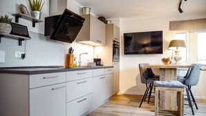 Una cocina moderna con armarios blancos, horno empotrado, microondas y un televisor de pantalla plana grande montado sobre la encimera.