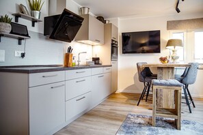 A modern kitchen with white cabinetry, a built-in oven, a microwave, and a large flat-screen TV mounted above the counter.
