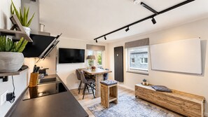 Una cocina moderna con un televisor de pantalla plana, un comedor con mesa y sillas de madera, y una zona de estar con un banco.