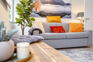 A modern living room with a grey sofa, a wooden coffee table, and a large window with a view of a mountain.