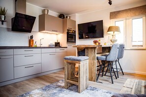 Une cuisine moderne avec des meubles blancs, un tabouret de bar en bois et un coin repas avec deux chaises.