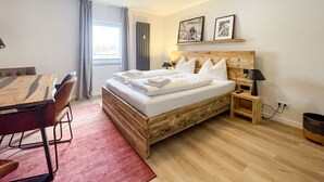 Habitación de hotel con cama de madera, un escritorio, una silla, un tapete rojo y una ventana con cortinas.