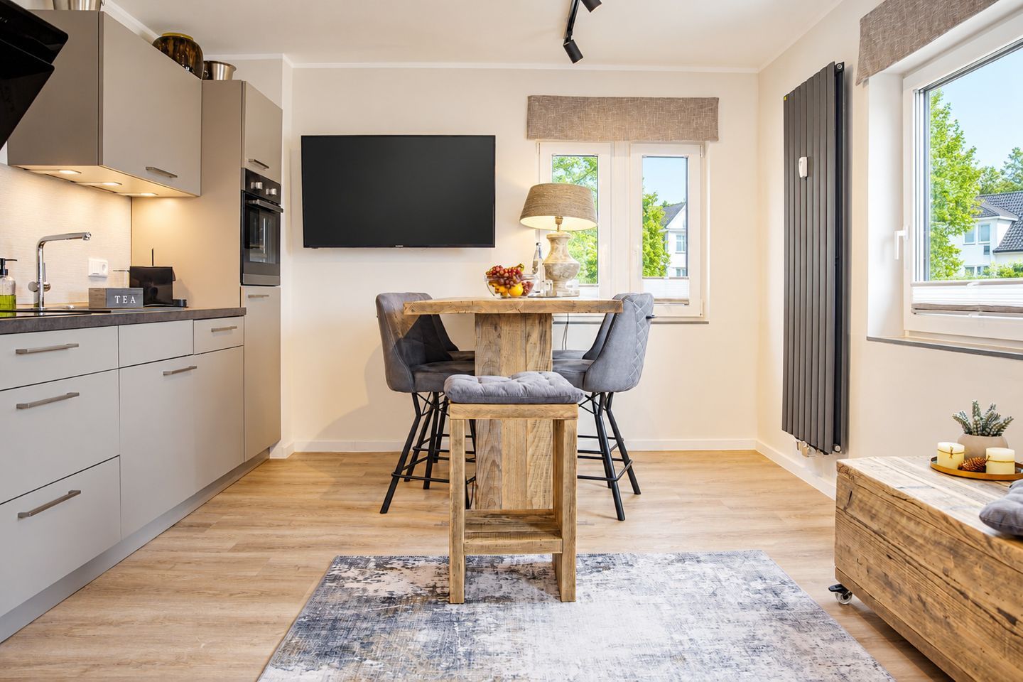 A modern kitchen with a flat-screen TV, wooden dining table, and bar stools.