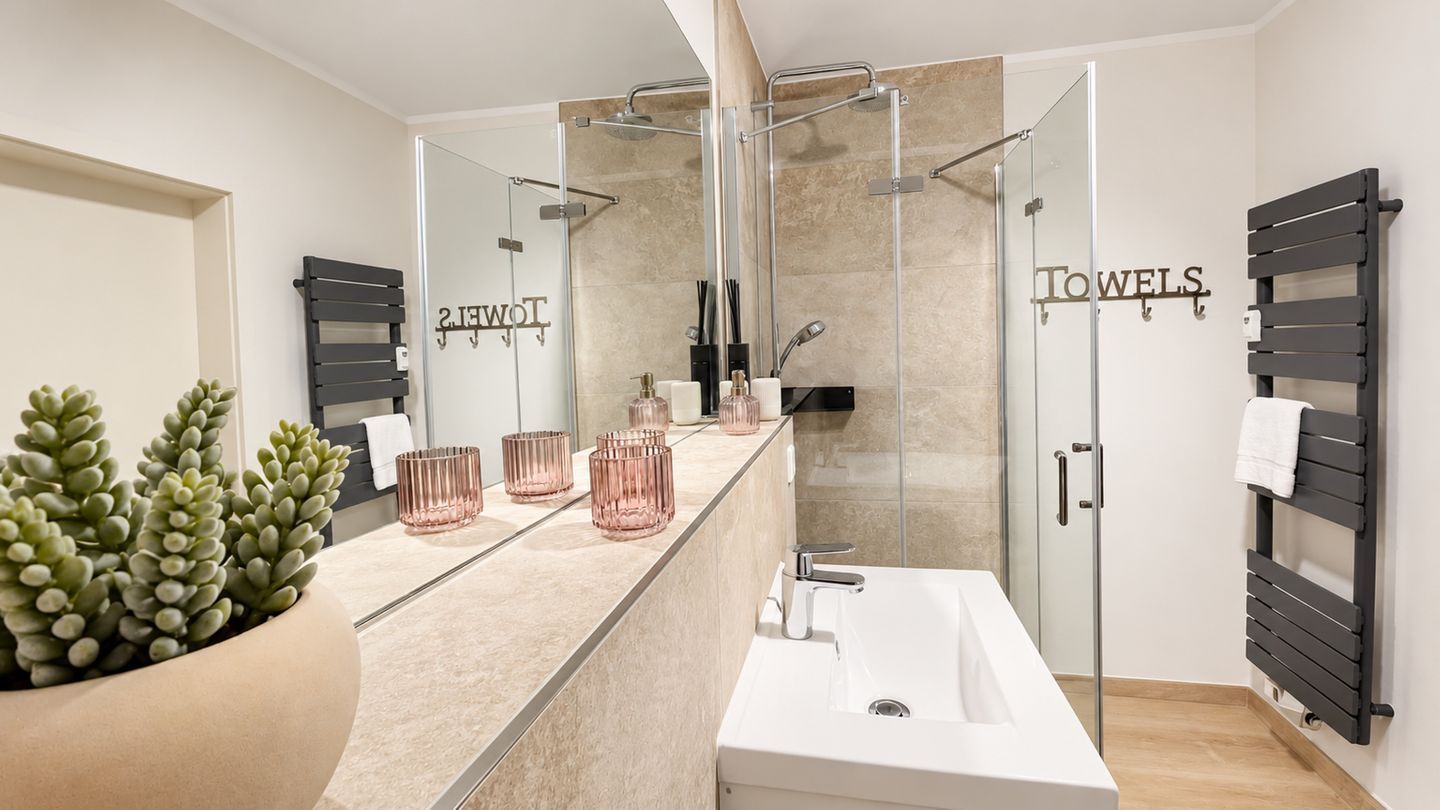 Ein modernes Badezimmer mit einem großen Spiegel, einem weißen Waschbecken und einer Duschkabine aus Glas.