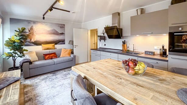 Una cocina moderna con una mesa de comedor de madera, un sofá gris y un frutero.