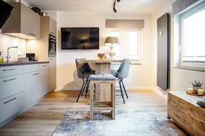 A modern kitchen with a dining area, wooden flooring, and a TV mounted on the wall. - Smart Resorts - Haus Topas - Ferienwohnung 302 mit 1 Schlafzimmer, Max. 4 Personen - Smart Resorts (Winterberg)