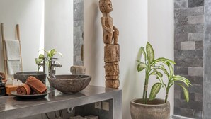 Ein modernes Badezimmer mit einem großen Spiegel, einer Steinwand und einer Holzskulptur.