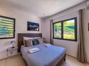 A hotel room with a bed, a nightstand, a wall-mounted picture, and a window with curtains.