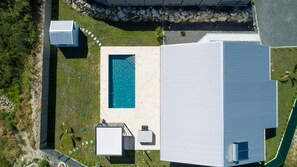 Oversigtsbillede af en ejendom med swimmingpool, en stor bygning og en stenvæg.