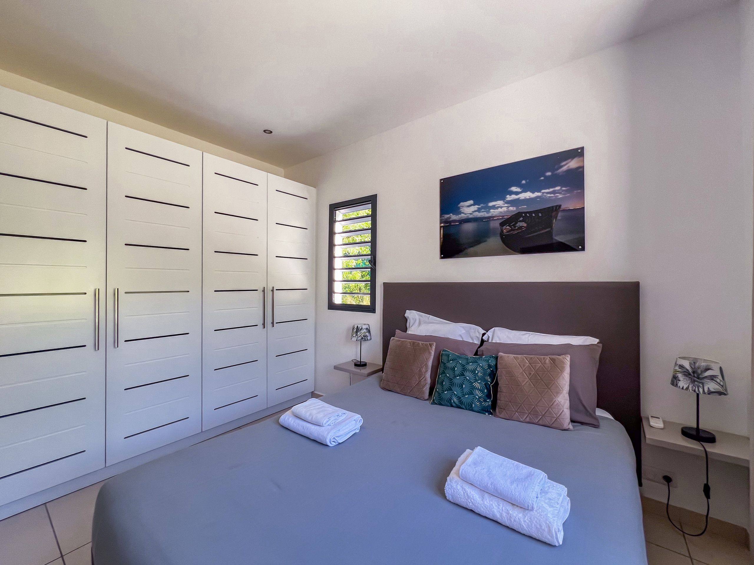 A bedroom with a large bed, a wardrobe, a nightstand, and a wall-mounted picture.