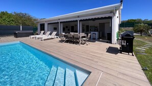Un espace aménagé au bord de la piscine, comprenant une piscine, des chaises longues, une table et un patio couvert.