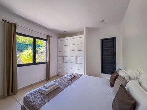 Un dormitorio con cama, armario, ventana con cortinas y vistas al exterior.