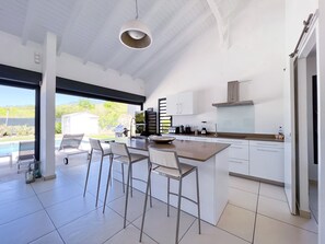 Une cuisine moderne dotée d’un grand îlot central, de tabourets de bar, d’un four encastré et offrant une vue sur une piscine.