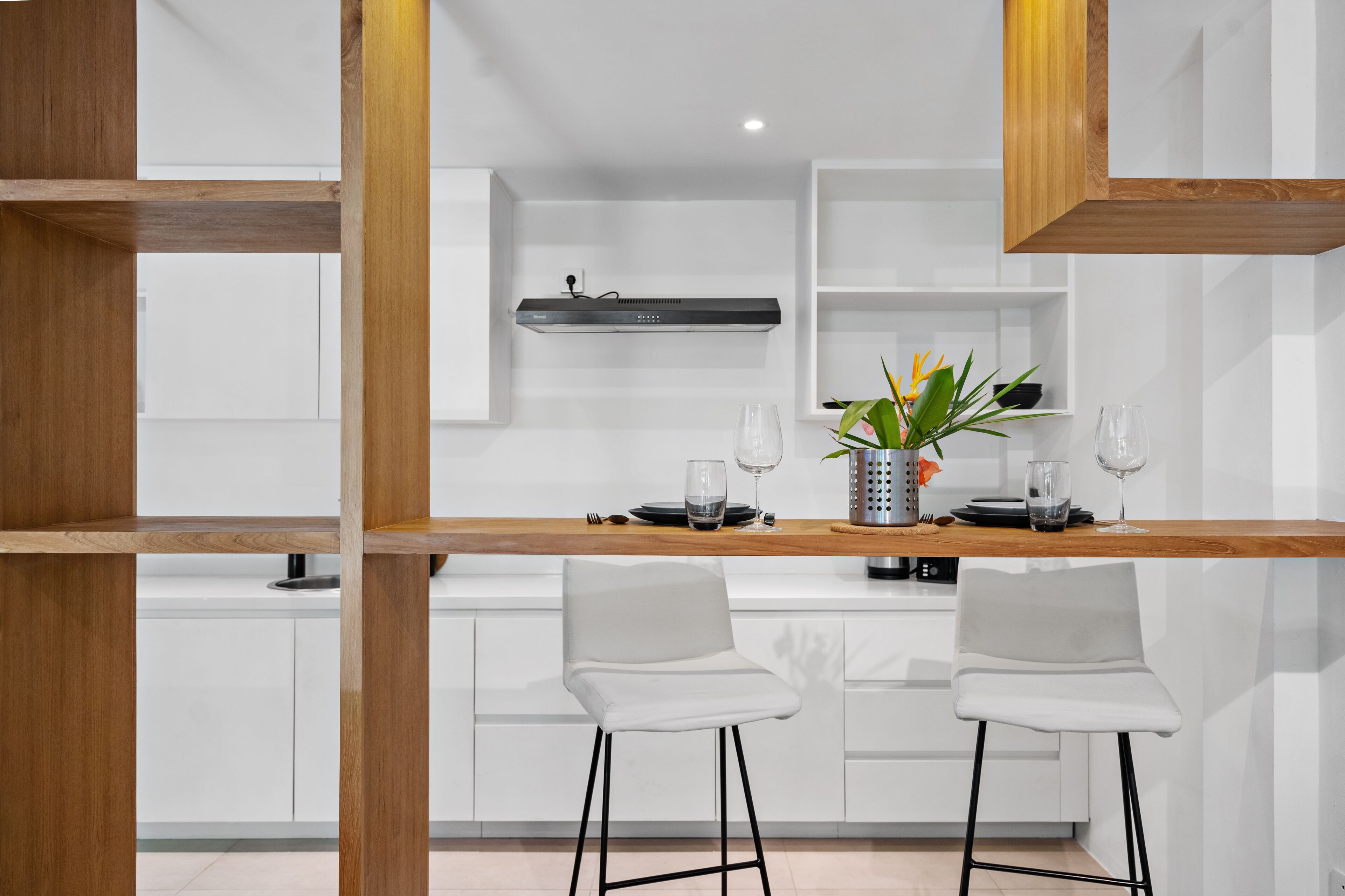A modern kitchen with white cabinetry, a wooden countertop, two white bar stools, and a built-in stainless steel range hood.