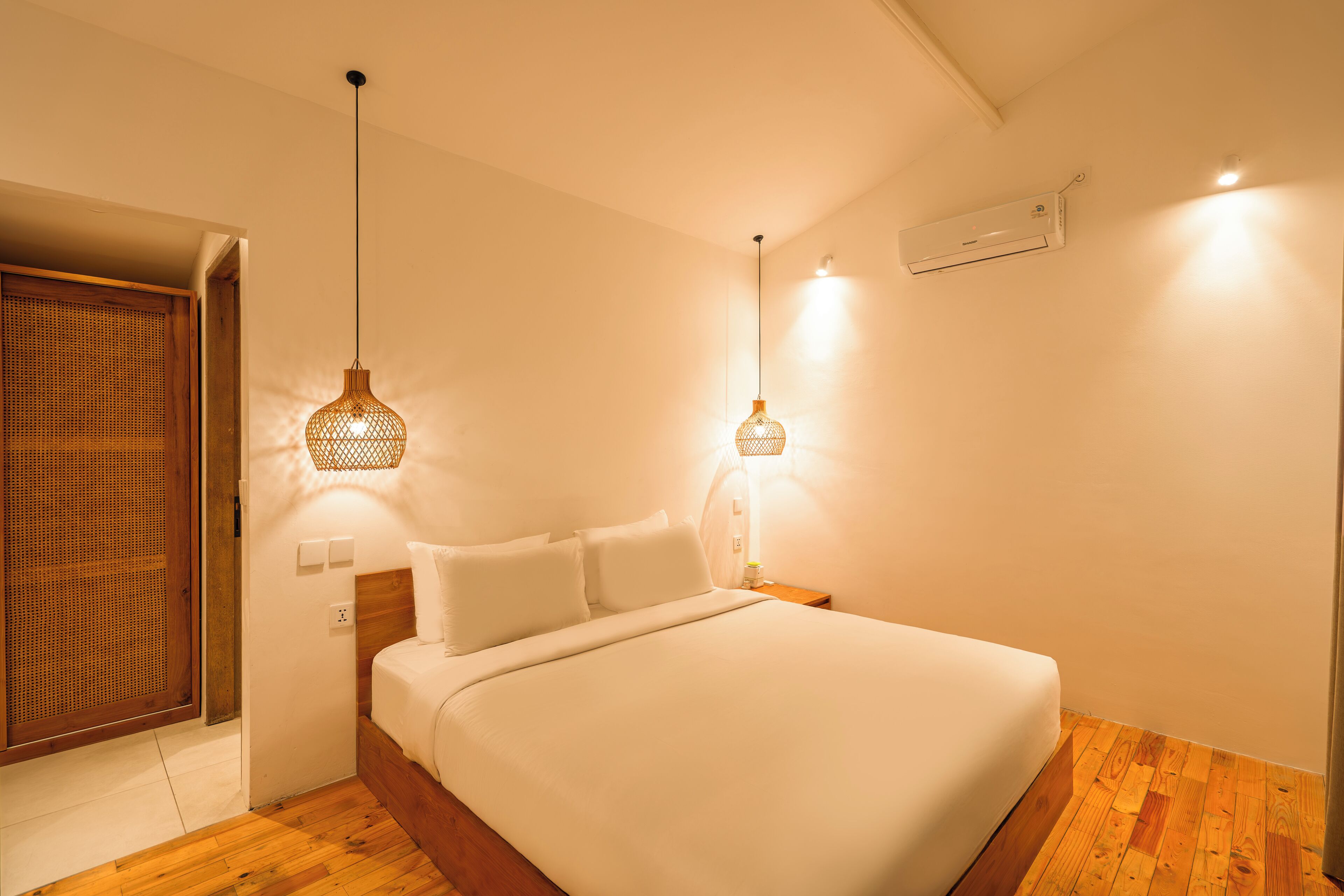 Un dormitorio con piso de madera, una cama con ropa blanca, dos lámparas de pared y un ventilador de techo.