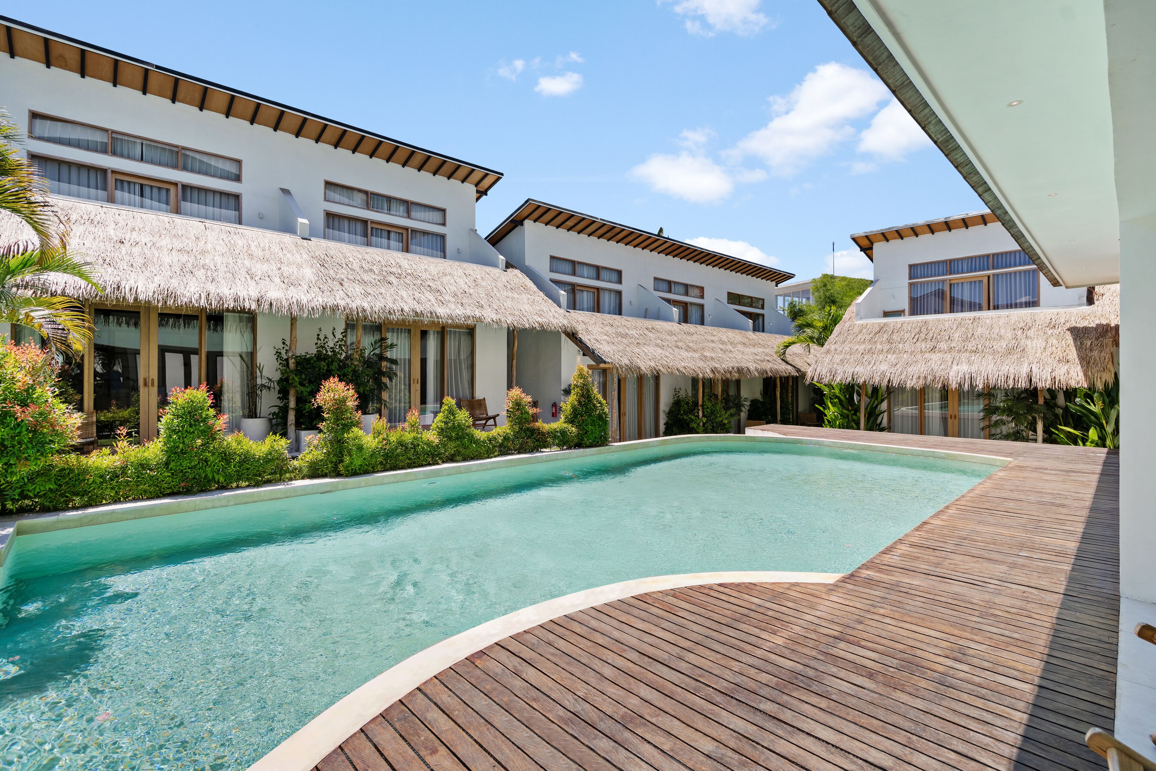 A resort with a swimming pool, thatched-roof buildings, and a wooden deck.