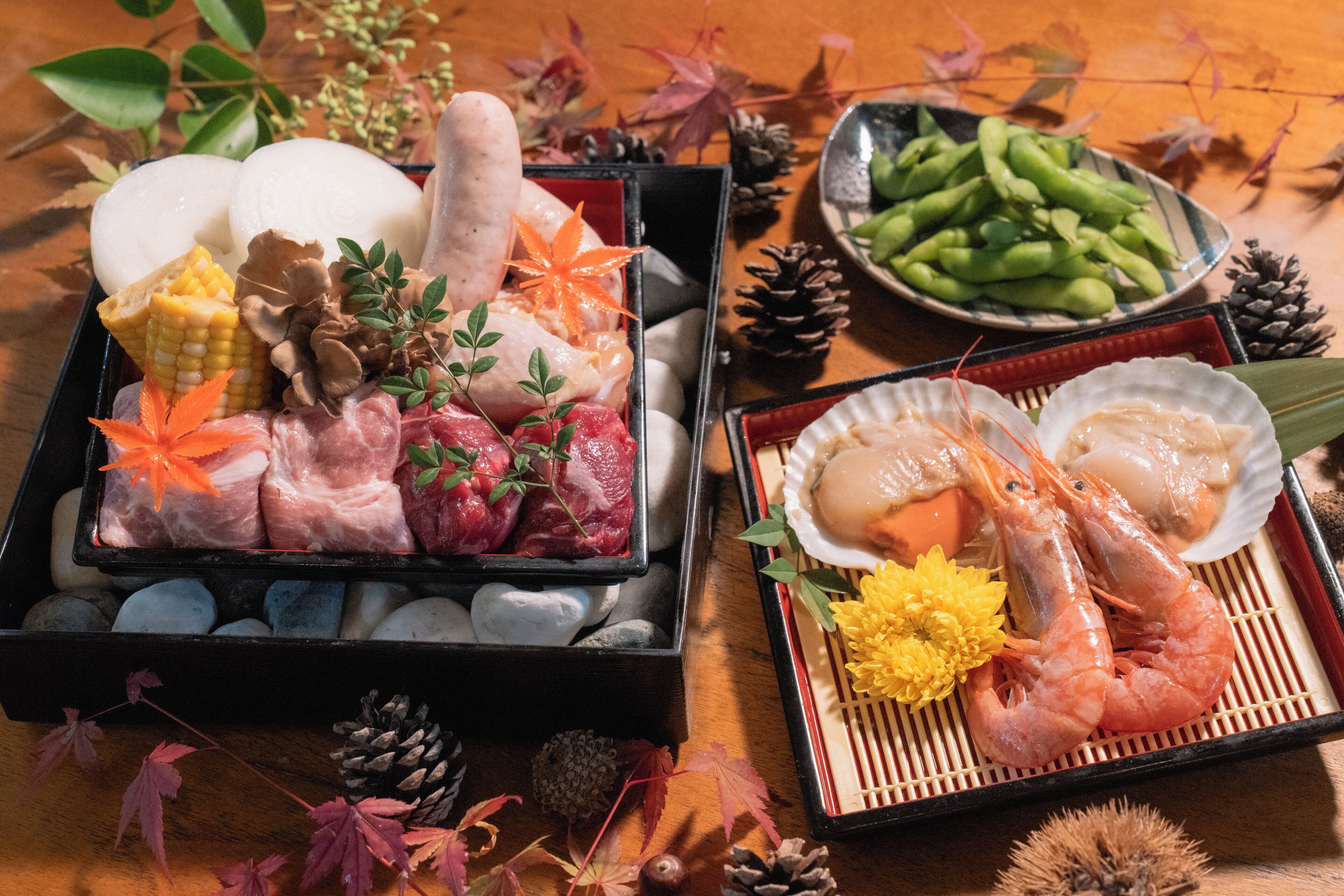 A traditional Japanese meal with various meats, seafood, and vegetables, presented on a wooden table with decorative elements.