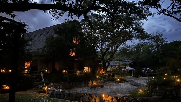 A rustic building with stone walls and a thatched roof, surrounded by trees and a small pond with a stone wall. - wood design park seto (Seto)