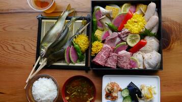 Une table en bois sur laquelle est servi un repas composé de poisson, de viande, de légumes et de riz, accompagné d’une tasse de thé.