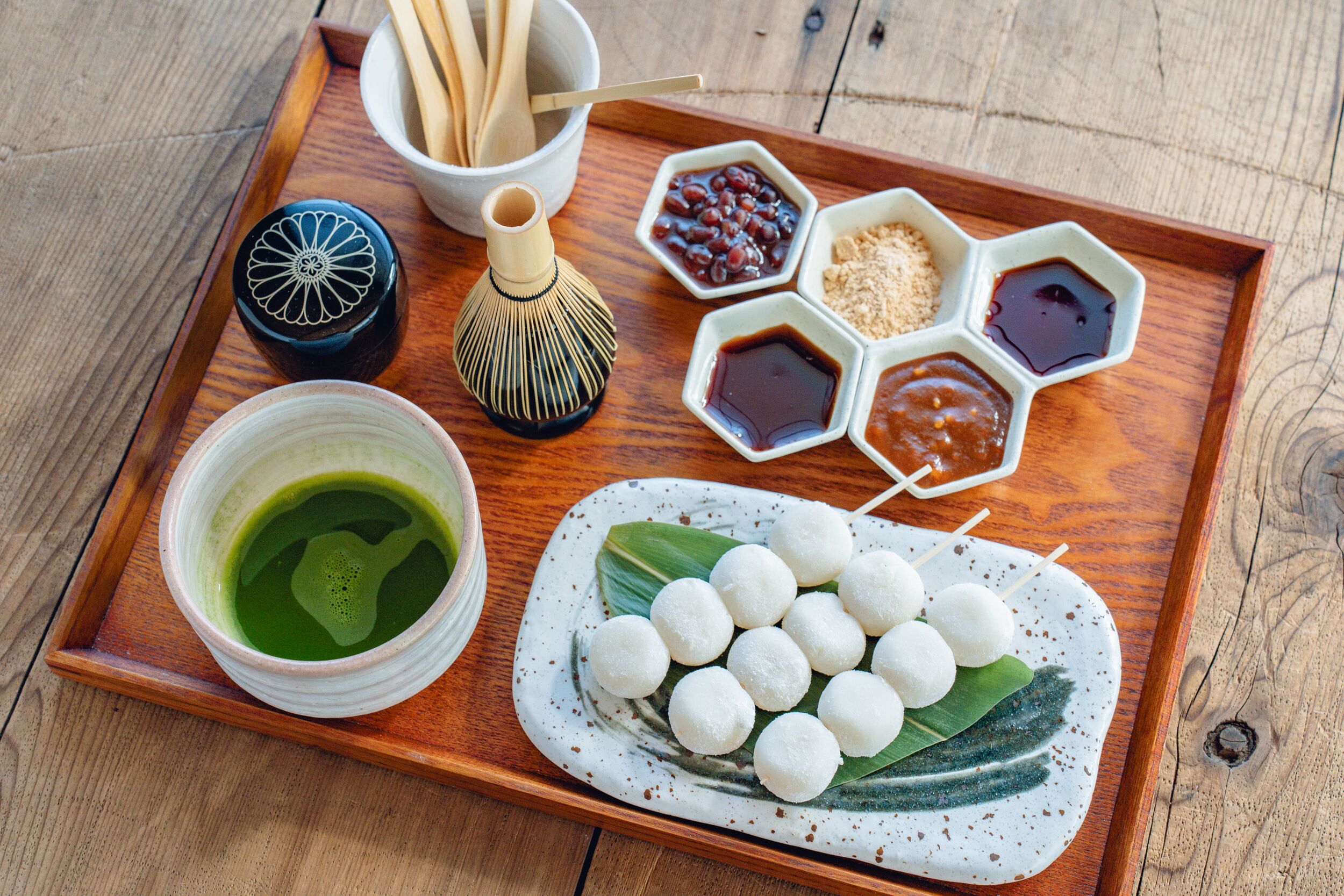 A wooden tray with a bowl of green tea, a bottle, and several small dishes containing different condiments.