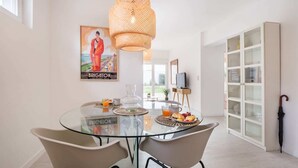 A modern dining area with a glass table, two chairs, a wicker pendant light, and a poster on the wall. - Seascape Apartment Unit 2 by Portugal Portfolio (Estoril)