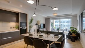 A modern kitchen with dark cabinetry, a dining area with a table set for four, and a large window offering a view of the city.