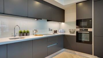 A modern kitchen with dark cabinetry, a stainless steel sink, a microwave, and an oven.