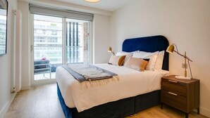 A bedroom with a bed, bedside table, lamp, and a view through a sliding door to an outdoor balcony. - The Benson Two by Dublin At Home (Dublin)