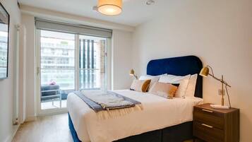 A bedroom with a bed, bedside table, lamp, and a view through a sliding door to an outdoor balcony.
