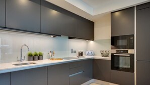 A modern kitchen with dark cabinetry, a stainless steel sink, a microwave, and an oven. - The Benson Two by Dublin At Home (Dublin)