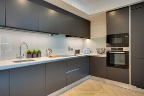 A modern kitchen with dark cabinetry, a stainless steel sink, a microwave, and an oven. - The Benson Two by Dublin At Home (Dublin)