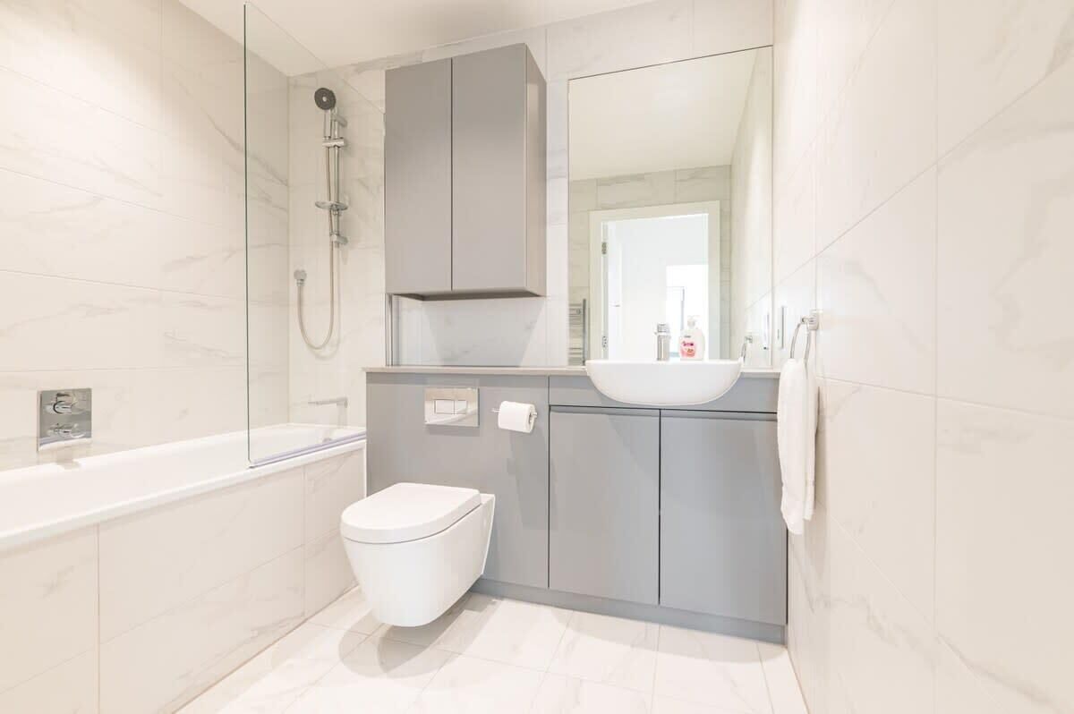 Une salle de bain moderne avec une douche à parois de verre, des toilettes blanches et un meuble-lavabo gris.