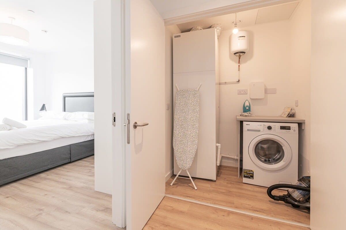 Une petite pièce comprenant un lit, un lave-linge et un étendoir.