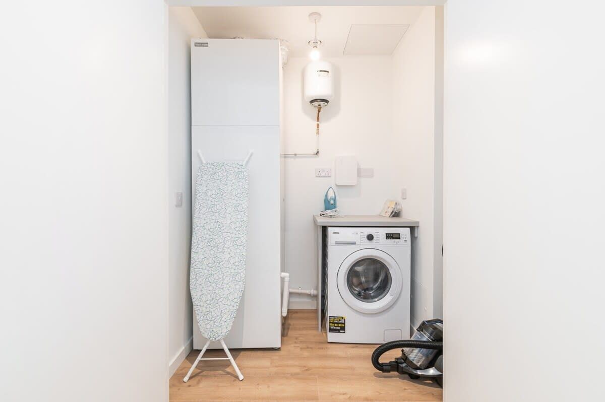 A compact laundry room with a washing machine, a drying rack, and a water heater.