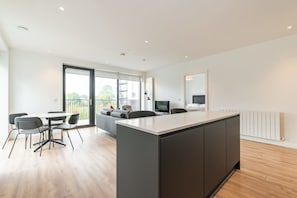 A modern kitchen with a central island, dining area with chairs, and a large window providing natural light.