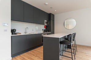 A modern kitchen with dark cabinets, a microwave, a coffee maker, and a round mirror on the wall.