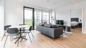 A modern living space with a sofa, dining table, chairs, a TV, and a bed.