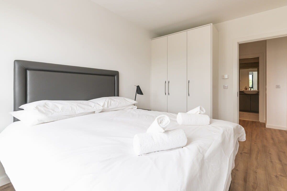 A neatly made bed with white linens and towels, a grey headboard, and a wardrobe with two doors.