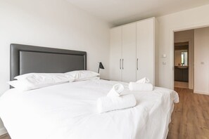 A neatly made bed with white linens and towels, a grey headboard, and a wardrobe with two doors.