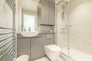 A modern bathroom with a glass-enclosed shower, a white sink, and a toilet.
