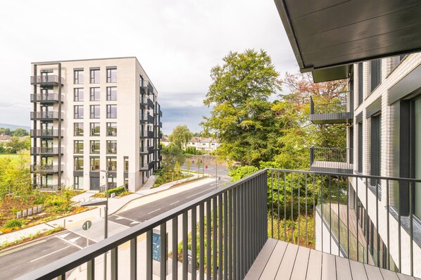 A modern apartment building with balconies, a street, and greenery.