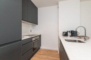 A modern kitchen with dark cabinets, a white countertop, a stainless steel sink, and a coffee maker.