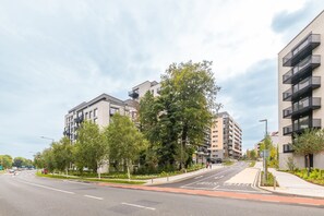 A modern urban street with multi-story residential buildings, a clear road, and a sidewalk with trees.