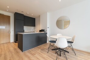 A modern kitchen with a central island, white dining table with chairs, and a round mirror on the wall. - Grange One Summary:<br>T (Dublin)