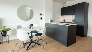 A modern kitchen with a central island, white dining chairs, a round mirror, and a potted plant. - City Apartments by Dublin At Home Two (Dublin 1)