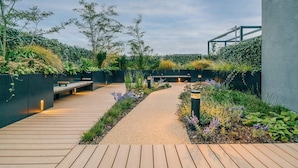 Un giardino pensile con un vialetto in legno, zone relax e diverse piante.