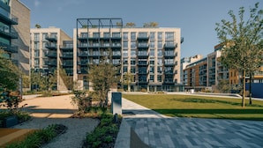 Un edificio moderno a più piani con balconi, un cortile lastricato e vegetazione circostante.